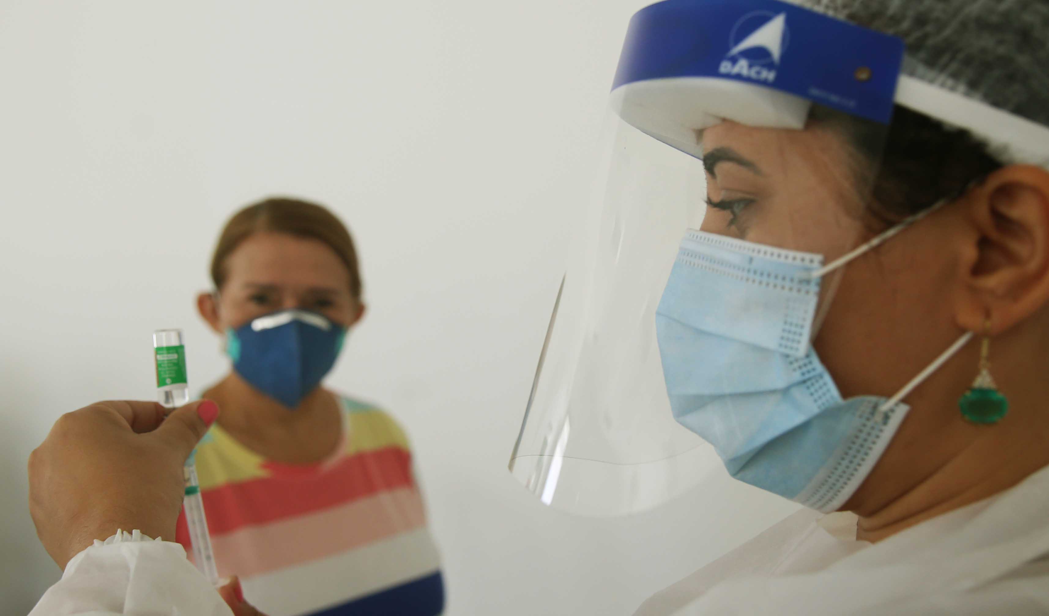 enfermeira ajusta uma seringa de vacinação, observada por uma idosa